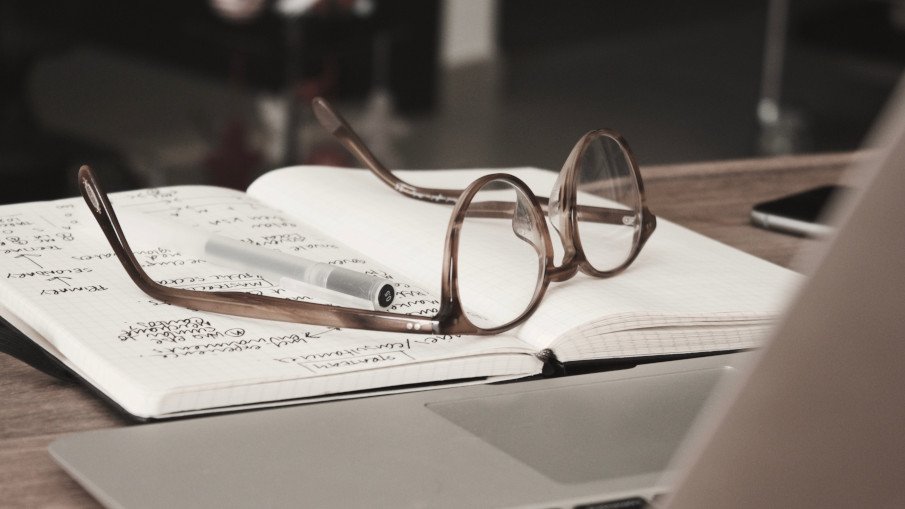 a pair of glasses and a pen over a notebook