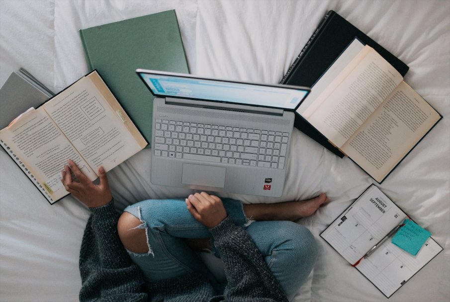 woman studying in her bed at home with her laptop and some books