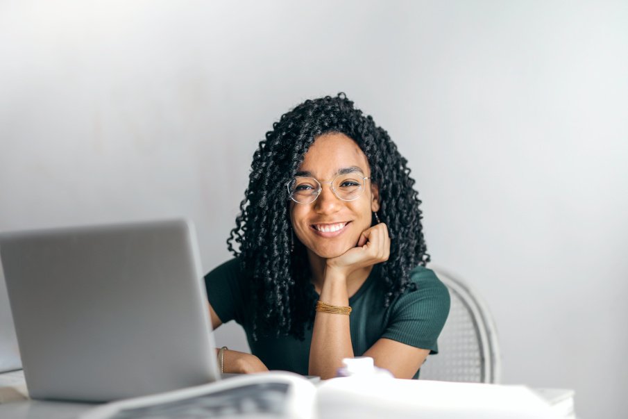 african woman sitting and smiling at the camera with a laptop in front of her
